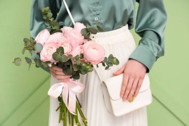 Yeşil arka planda bir buket ranunculus çiçeği ve okaliptüs olan genç kadın, yakın plan.