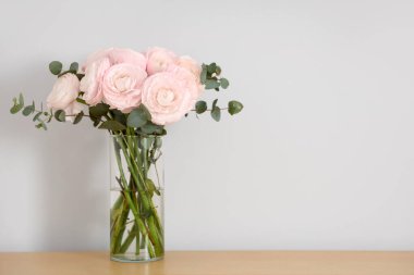 Bej duvarın yanındaki masada bir buket güzel ranunculus çiçeği olan vazo, yakın plan.