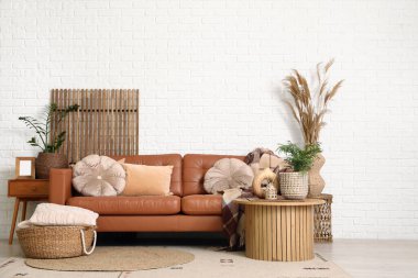 Oturma odasının iç tarafındaki beyaz tuğla duvarın yanında katlanan ekran ve deri kahverengi kanepe.