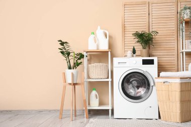 Modern çamaşır makinesi, sepet, raf ünitesi ve deterjan şişeleriyle şık bir çamaşır odası.