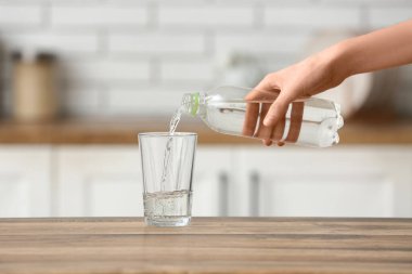 Kadın mutfaktaki ahşap masaya şişeden cama su döküyor.