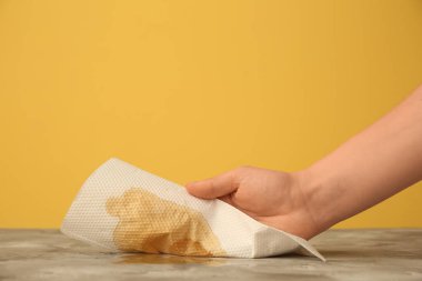 Sarı duvarın yanındaki grunge gri masaya kağıt peçeteyle kahve döken kadın.