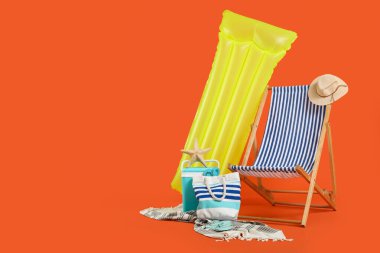 Şişme şiltesi, plaj soğutucusu ve turuncu arka planda yaz aksesuarları olan bir şezlong. Tatil kavramı