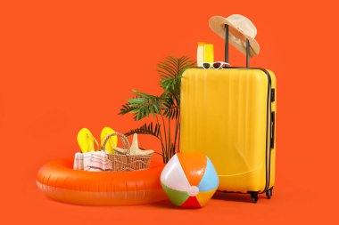 Şişme yüzüklü bavul, yaz çantası, güneş kremi ve turuncu arka planda plaj aksesuarları. Tatil kavramı