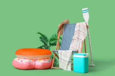 Şişirilebilir yüzüklü iskemle, plaj soğutucusu, kürek ve yeşil arka planda yaz aksesuarları. Tatil kavramı