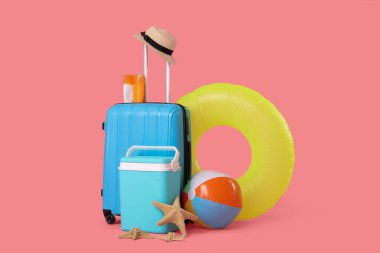 Şişme yüzüklü bavullar, plaj soğutucusu, güneş kremi ve pembe arka planda yaz aksesuarları. Tatil kavramı