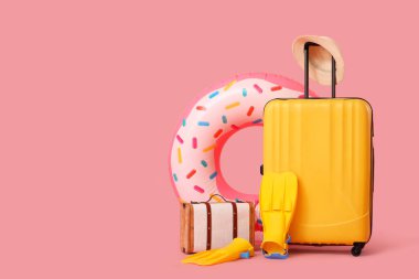Şişme yüzüklü bavullar, paletler ve pembe arka planda plaj aksesuarları. Tatil kavramı