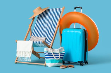 Bavullu iskemle, şişme yüzük, yaz çantası ve mavi arka planda plaj aksesuarları. Tatil kavramı
