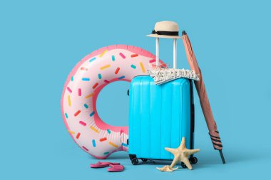 Şişme yüzüklü bavul, plaj şemsiyesi ve mavi arka planda yaz aksesuarları. Tatil kavramı