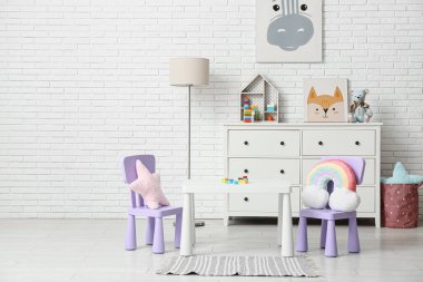 Çocuk odasının içinde lamba, oyun masası, beyaz tuğla duvarın yanında bir sürü oyuncak.