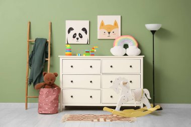 Çocuk odasının içinde lamba, merdiven, sallanan at ve yeşil duvarın yanında bir sürü oyuncak var.