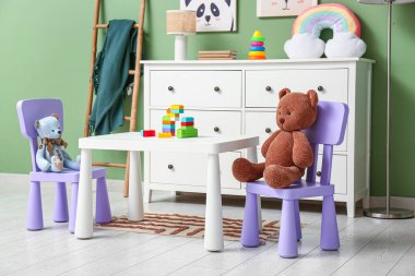 Çocuk odasının içinde lamba, merdiven, oyun masası ve yeşil duvarın yanında bir sürü oyuncak var.