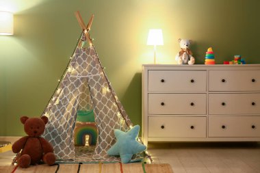 Gece çocuk odasının içinde parlayan lambalar, yeşil duvarın yanında çadır ve oyuncaklar var.