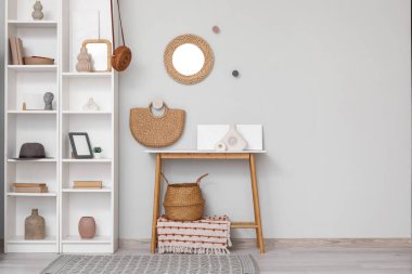 Oturma odasının içinde, masası, asılı aynası ve gri duvarın yanındaki raf ünitesinde dekorasyonu var.