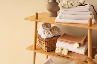 Raflar temiz yatak çarşafları, pamuk çiçekleri ve bej duvarın yanındaki ev dekoruyla dolu.