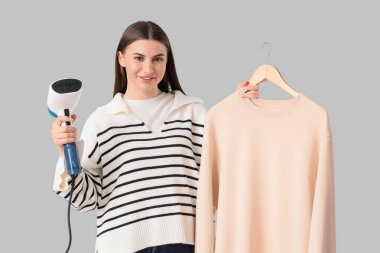 Gri arkaplanda buharlı kazağı olan güzel, mutlu bir kadın.