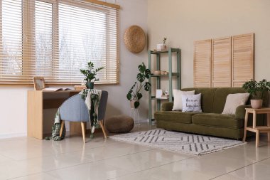 Oturma odasının içinde kanepe, raf ünitesi, işyeri ve penceresinde ahşap panjurlar var.