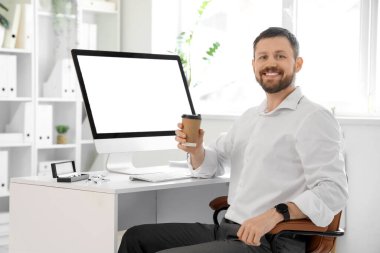 Ofiste kahve fincanı ve boş bilgisayarla çalışan genç bir işadamı.