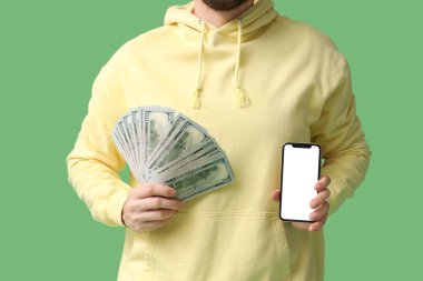 Cep telefonu ve yeşil arka planda parası olan genç adam, yakın plan. Spor bahsi konsepti