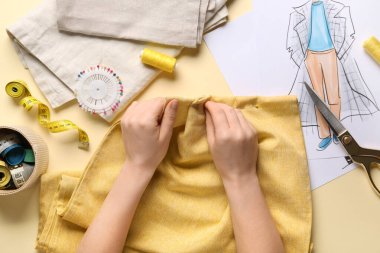 Kadın elleri arka planda sarı elbiseler dikiyor.