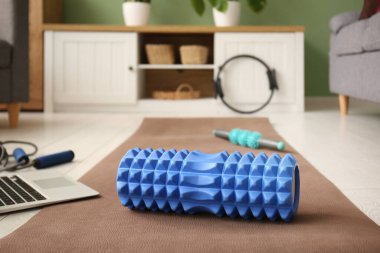 Oturma odasındaki yoga minderinde dizüstü bilgisayarı ve spor malzemesi olan köpük silindirli.