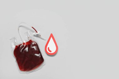 Gri arka planda kırmızı kağıt damlalarıyla kan nakli için kan torbası. Kan bağışı konsepti