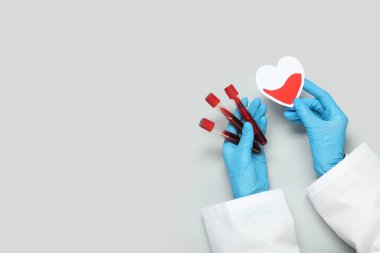Kağıt kalpli kadın doktor elleri ve gri arka planda kan tüpleri. Kan bağışı konsepti