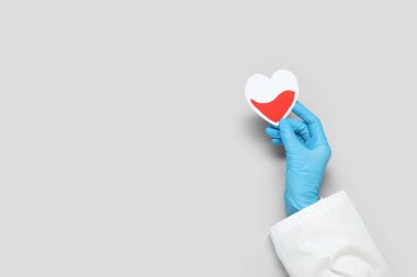 Gri arka planda kağıt kalpli bir kadın doktor eli. Kan bağışı konsepti