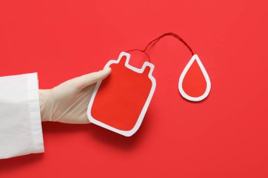 Kadın doktor eli kağıt kan torbası ile kırmızı arka plana düşmüş. Kan bağışı konsepti