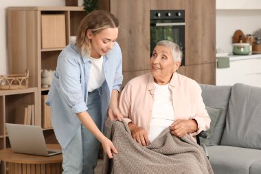 Genç bir kadın evde büyükannesini sıcak bir ekoseyle örtüyor.