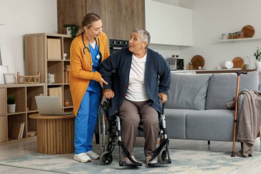 Genç bakıcı ve yaşlı kadın evde tekerlekli sandalyede oturuyor.