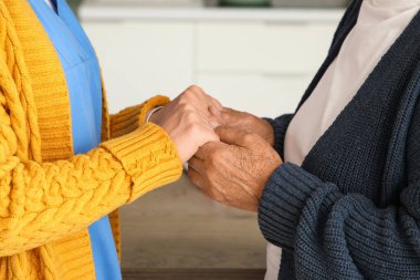 Mutfakta el ele tutuşan yaşlı bir kadınla genç bakıcı, yakın plan.