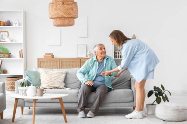 Young woman helping her grandmother to stand up from sofa at home