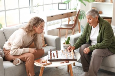Torunuyla evde satranç oynayan yaşlı bir kadın.