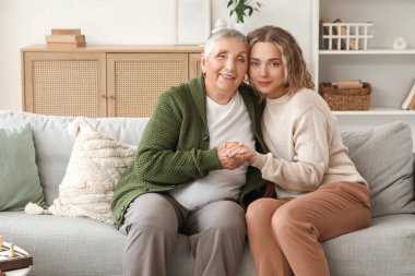 Torunuyla birlikte evdeki koltukta el ele tutuşan son sınıf öğrencisi kadın.