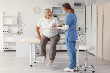 Klinikte hemşireyle el ele tutuşan kıdemli kadın.