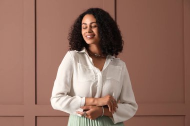 Kahverengi duvarın yanında gümüş mücevherleri olan genç bir Afro-Amerikalı kadın.