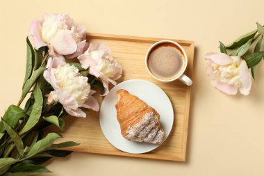 Tatlı kruvasanla güzel şakayık çiçekleri ve bej arka planda bir fincan kahve.