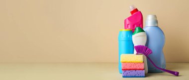 Bej arka planda temizlik malzemeleri ve şişe deterjan var.