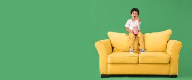 Kanepedeki izleyiciyi işaret eden patlamış mısırlı şaşkın çocuk yeşil arka planda mesaj için yer var.