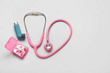 Astım spreyi, steteskop ve gri arka planda bir kutu hap.