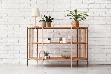 Odada beyaz tuğla duvarın yanında çiçek ve lamba olan masa.