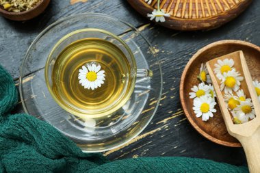 Siyah ahşap arka planda kurutulmuş papatya çayı ve kase.