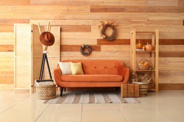 Oturma odasının içinde kahverengi kanepe, raf, çelenk ve balkabakları raflarda.