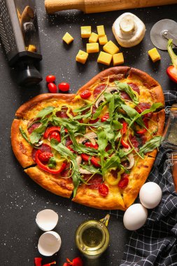 Lezzetli kalp şeklinde pizza. Siyah arka planda malzemeler var.