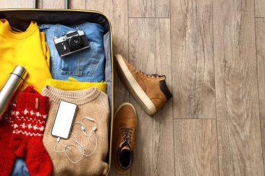 Giysilerle dolu bavul, cep telefonu ve ahşap zeminde fotoğraf makinesi.