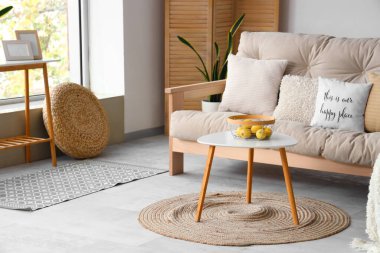 Beyaz kanepe ve sehpanın üzerinde meyve sepetiyle aydınlık oturma odasının içinde.