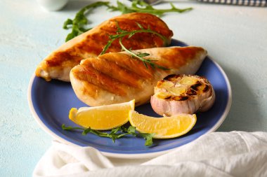 Lezzetli ızgara tavuk göğsü, sarımsak, roka ve açık mavi arka planda limon.