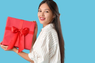 Mavi arka planda hediye kutusu olan güzel bir Asyalı kadın.
