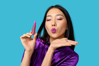 Beautiful Asian woman with lipstick blowing kiss on blue background